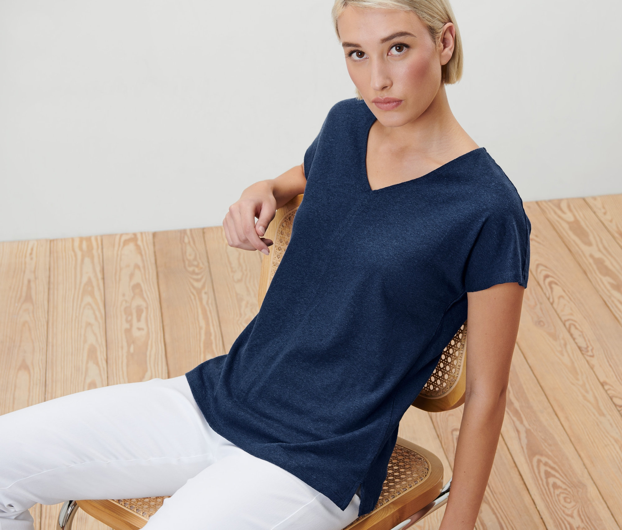 Blonde Frau sitzt auf einem Stuhl und trägt ein dunkelblaues Shirt mit Leinen.