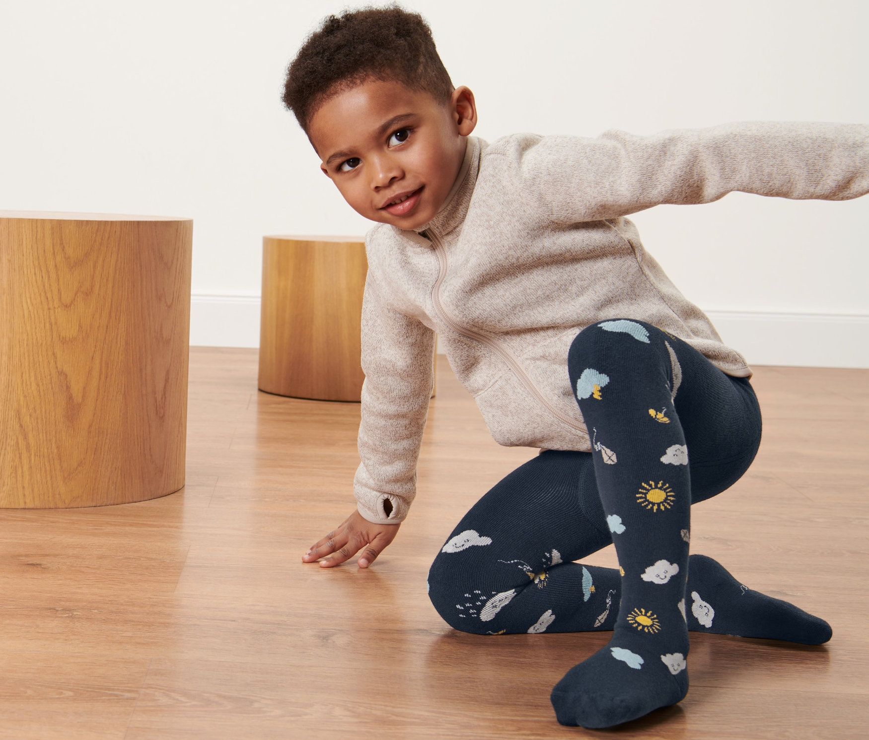 Junge kniet auf dem Boden und trägt eine Thermostrumpfhose mit Wolkenmuster.