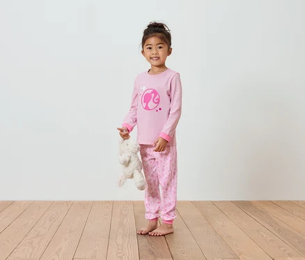 Mädchen im rosa Barbie-Pyjama hält einen Teddybären.