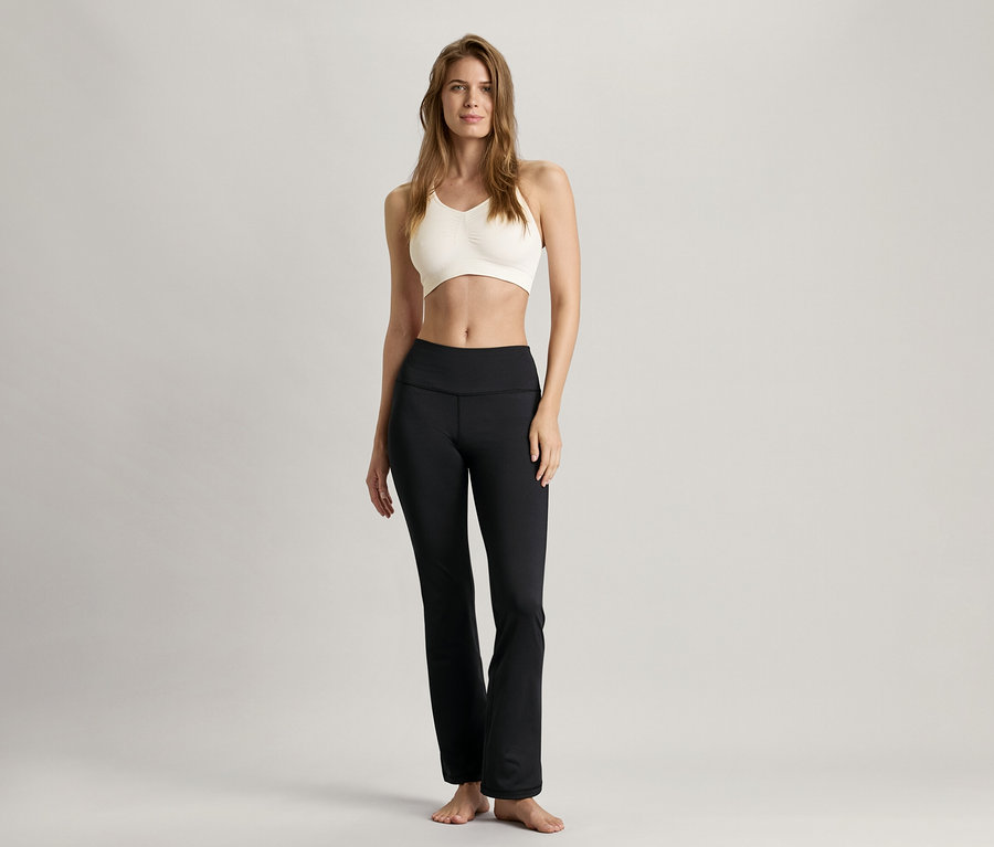 Frau steht und trägt ein Seamless-Sport-Bustier, weiß und eine schwarze Hose.