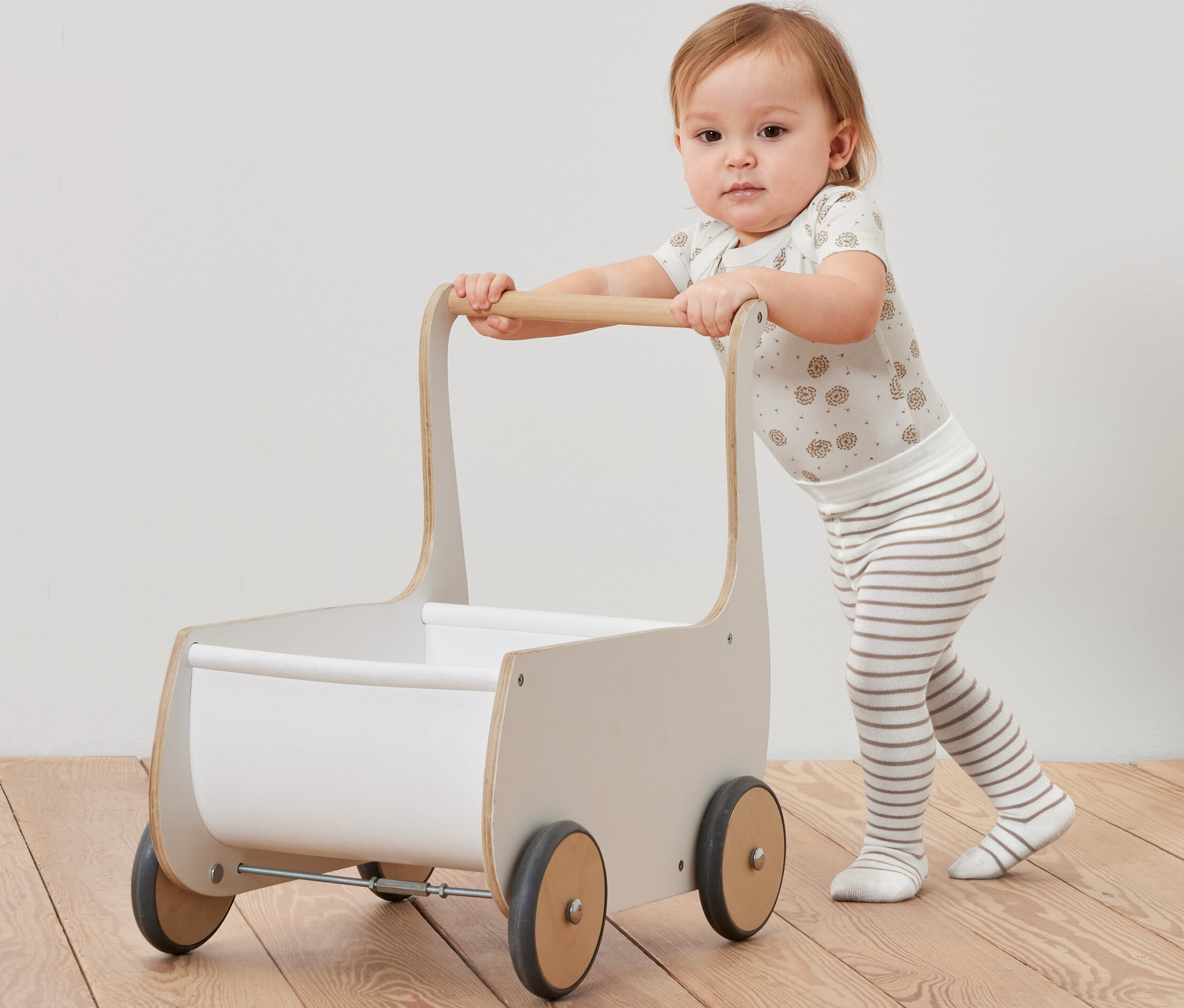 Ein Kleinkind schiebt einen Holzwagen und trägt eine Strumpfhose von 5 Paar Baby-Strumpfhosen.
