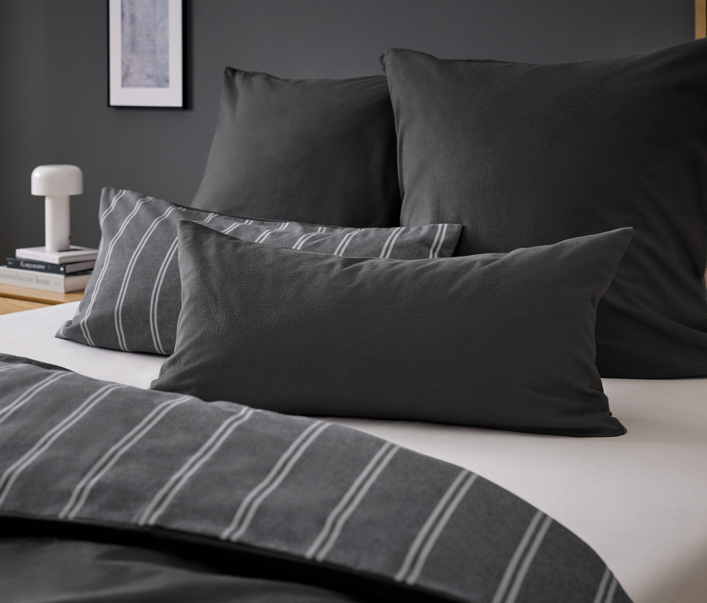 Vier graue Kissen auf einem Bett mit grau gestreifter Bettwäsche.