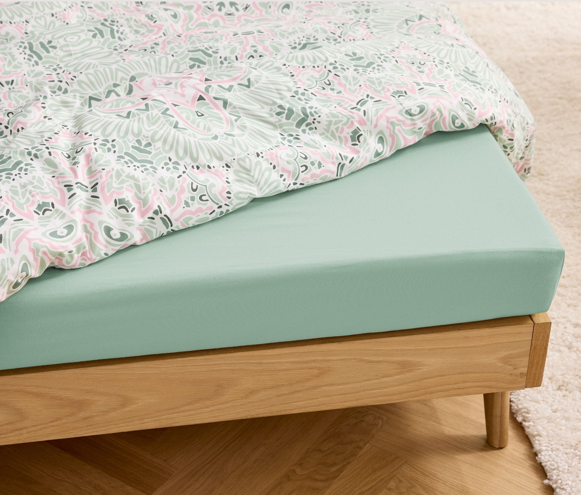 Ein hellgrünes Jersey-Spannbettlaken auf einem Bett mit Holzrahmen.