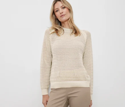 Blonde Frau posiert in einem Pullover in Pointellestrick und Hose.