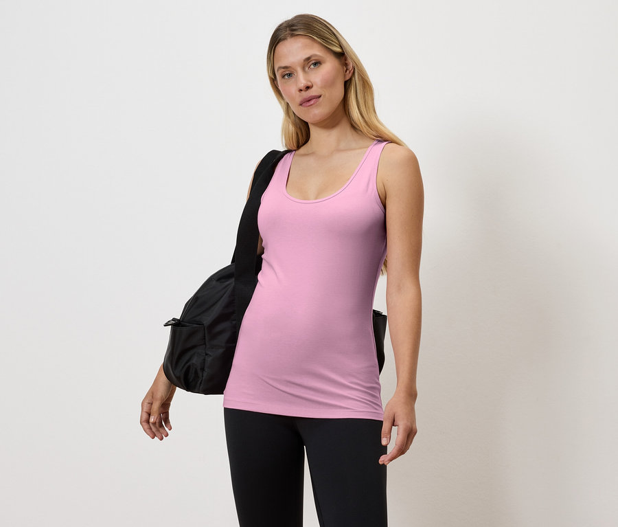 Frau in rosa Tanktop und schwarzen Leggings mit schwarzer Tasche über der Schulter.