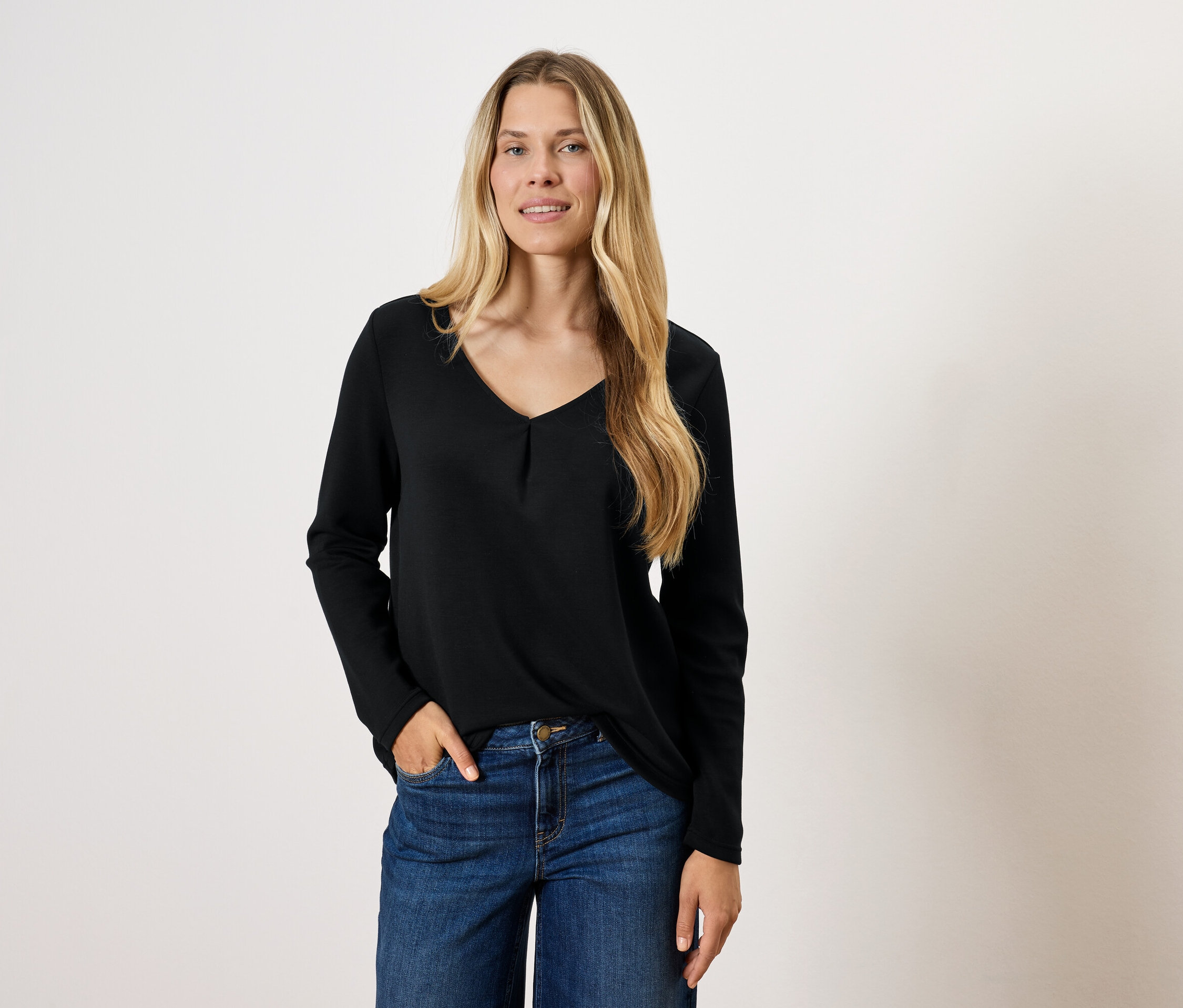 Blonde Frau in schwarzem Langarmshirt und blauen Jeans posiert.