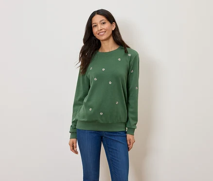 Frau trägt einen grünen Pullover mit Blumenmuster und blaue Jeans.
