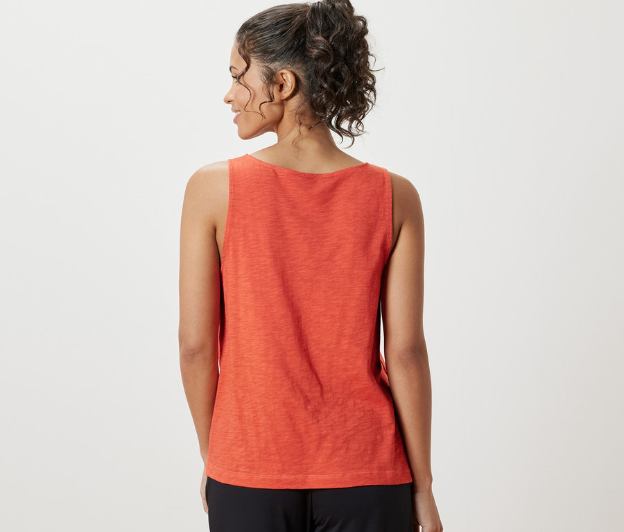 Frau trägt ein orangefarbenes Top aus Modalmix und eine schwarze Hose.