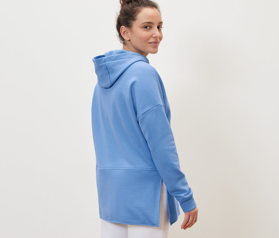 Frau blickt über die Schulter und trägt ein hellblaues langes Kapuzensweatshirt.