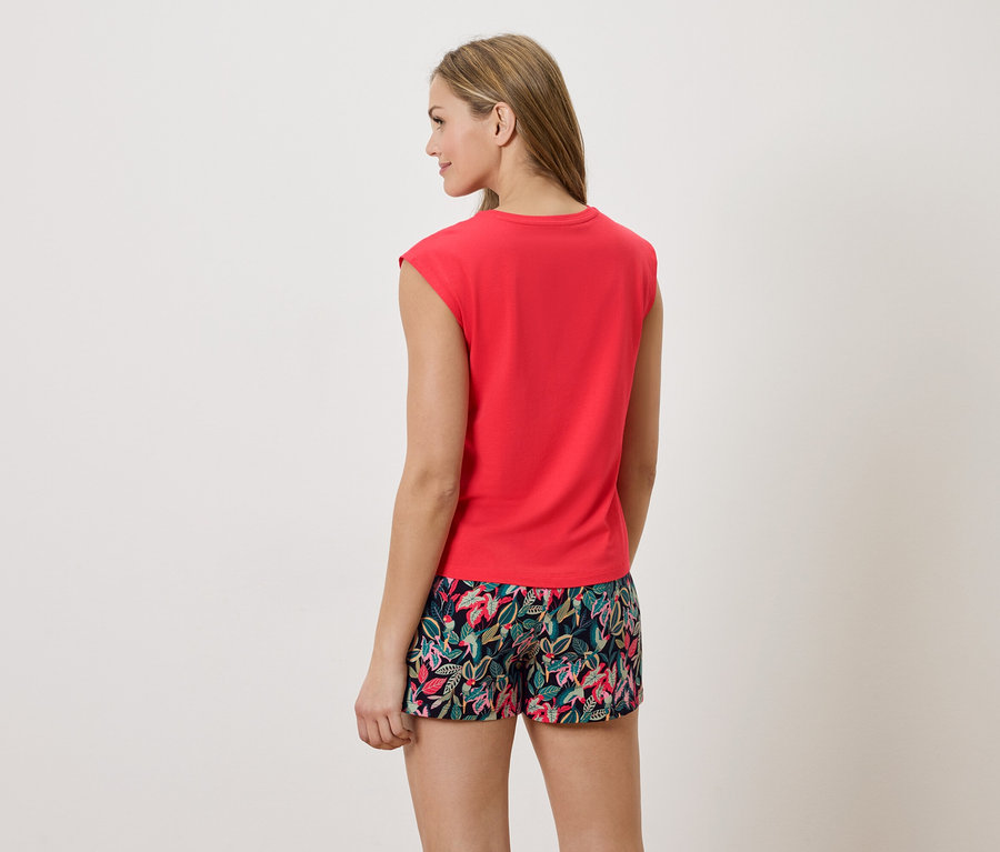 Frau von hinten, trägt ein rotes T-Shirt und Shorts mit Blumendruck.