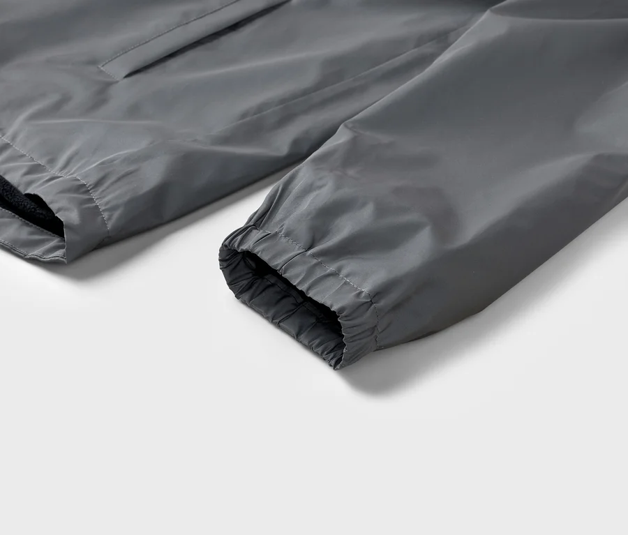 Detailaufnahme eines grauen Jackenärmels mit elastischem Bündchen vor einem weißen Hintergrund.