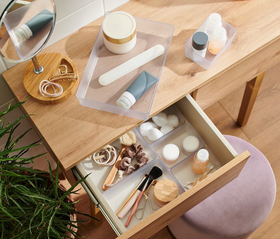Kosmetiktisch mit offenem Schubfach und verschiedenen Kosmetikprodukten, darunter Cremes, Tuben und Make-up-Zubehör.