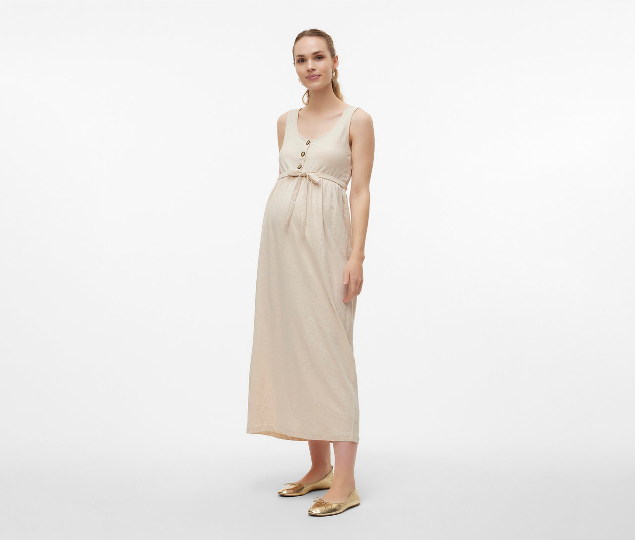 Frau trägt MAMALICIOUS Schwangerschaftskleid »MLEVI LIA« mit Gürtel und goldene Ballerinas vor hellem Hintergrund.