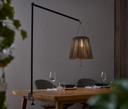 Esstisch mit Geschirr und Lampe mit schwarzem Lampenschirm, die an einer schwarzen Stange befestigt ist.