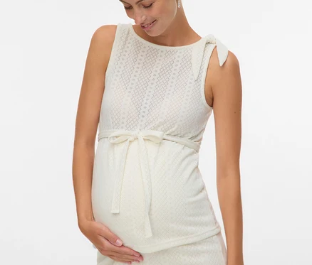 Eine schwangere Frau in einem ärmellosen Kleid mit Schleife und Muster berührt ihren Bauch.
