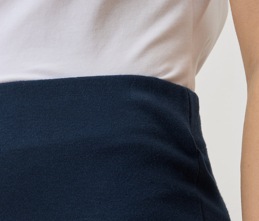 Nahaufnahme eines Teils des Oberkörpers einer Person, die ein weißes T-Shirt und einen marineblauen Rock trägt.