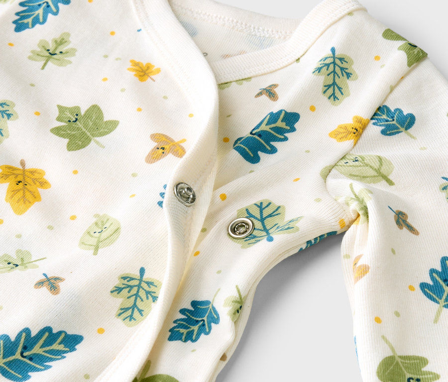 Nahaufnahme eines weißen Baby-Stramplers mit bunten Blättern und Druckknöpfen.