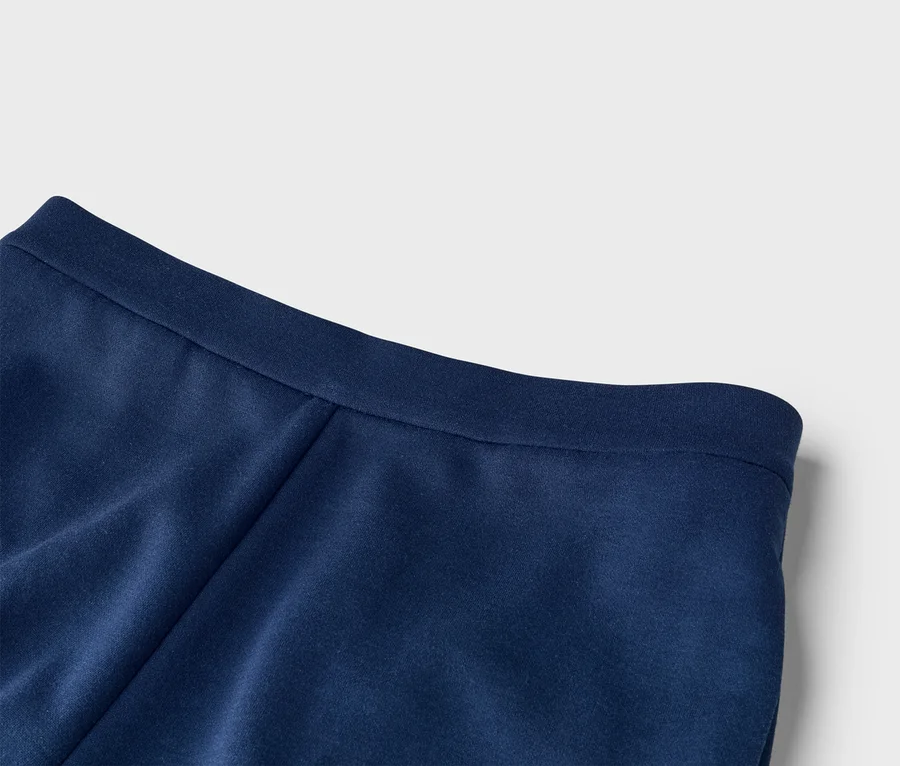 Nahaufnahme eines marineblauen Stoffes, der eine glatte Textur und einen flachen Bund oder Saum am oberen Rand zeigt. Der Stoff weist leichte Falten auf.