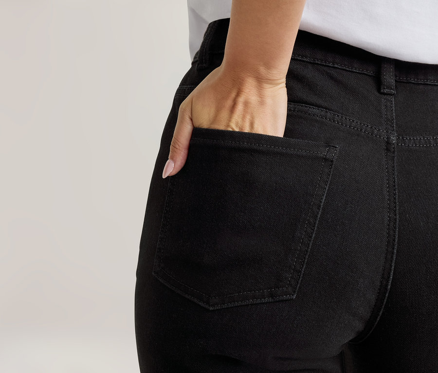 Eine Hand steckt teilweise in der Gesäßtasche einer schwarzen Jeans, von hinten gesehen.