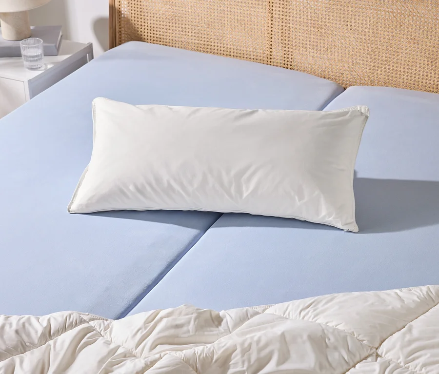 Ein Bett mit hellblauem Spannbettlaken, einem weißen Kissen und einer weißen Bettdecke. Daneben steht ein weißer Nachttisch mit Lampe und Wasserglas.