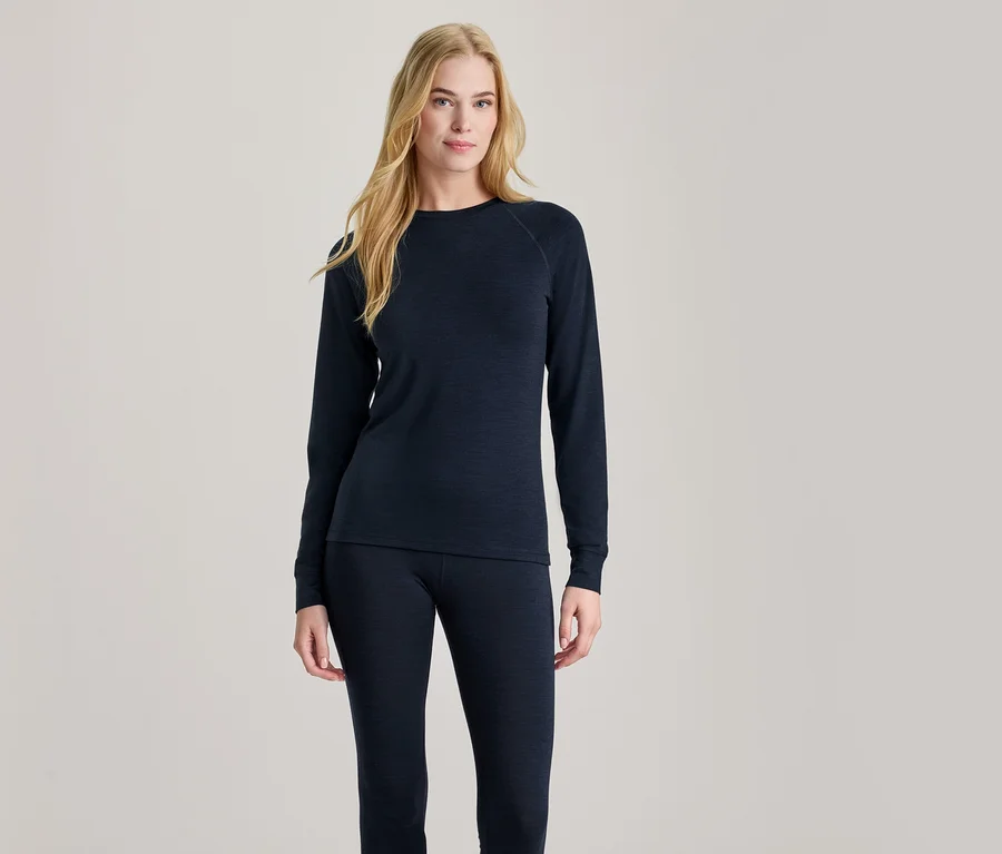 Blonde Frau steht da und trägt ein dunkelblaues Langarmshirt und passende dunkelblaue Leggings, blickt nach vorne.