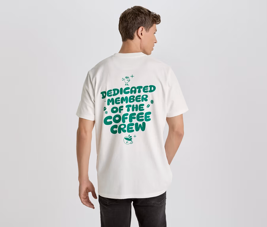 Ein Mann von hinten trägt ein weißes T-Shirt mit grünem Aufdruck 'Dedicated Member of the Coffee Crew'.
