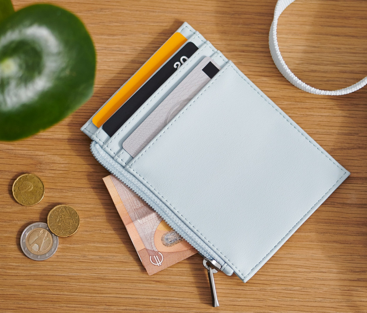 Auf einem Holztisch liegen ein hellblaues Portemonnaie, Münzen und eine Tasche.