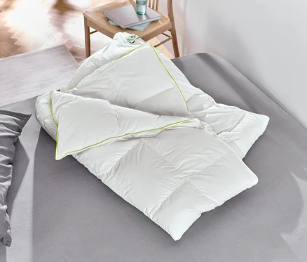 Eine weiße irisette® Übergangs-Daunendecke liegt auf einem Bett.