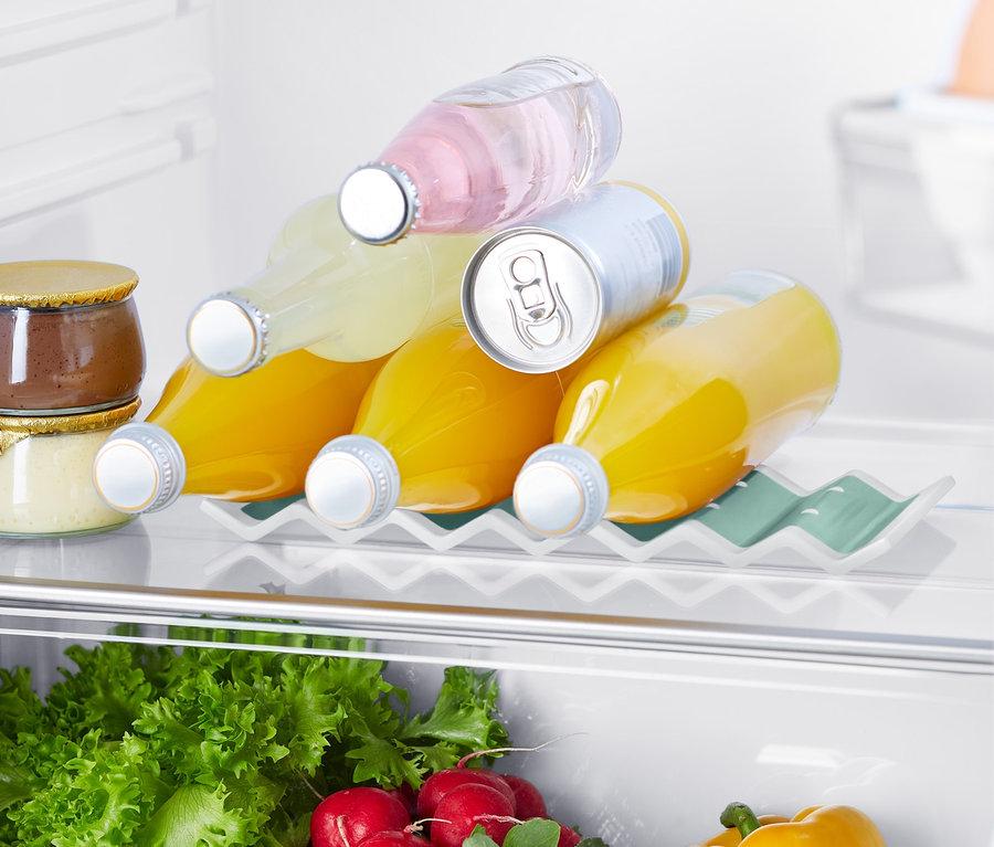 Im Kühlschrank befindet sich ein Kühlschrank-Flaschenhalter, auf dem drei Saftflaschen und eine Dose liegen. Im unteren Bereich sind Salate, Radieschen und eine gelbe Paprika zu sehen.