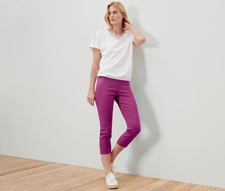 Frau posiert in einer 7/8-Stretchhose in Berry-Farbe, einem weißen T-Shirt und Turnschuhen.