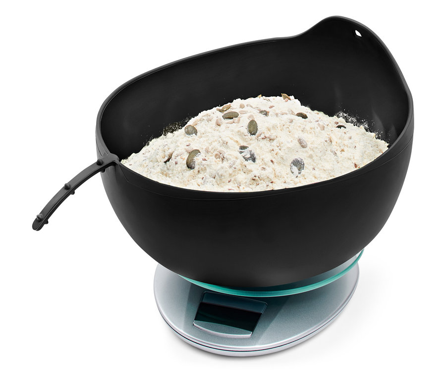 Eine schwarze Schüssel mit Mehl und Samen auf einer digitalen Waage.