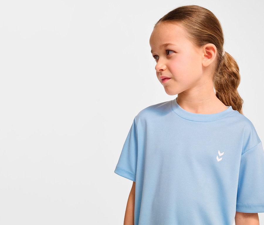 Mädchen trägt hellblaues HUMMEL HMLJR pulse Trainings-T-Shirt und schaut nach rechts.