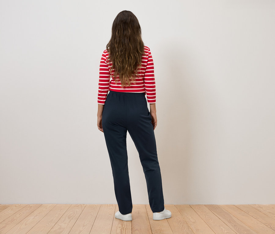 Frau mit rot-weiß gestreiftem Oberteil und dunkelblauer Hose steht mit dem Rücken zur Kamera.
