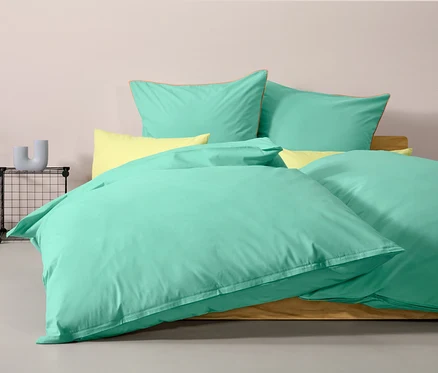 Türkise Renforcé-Bettwäsche Normalgröße auf einem Bett mit gelben Kissen.