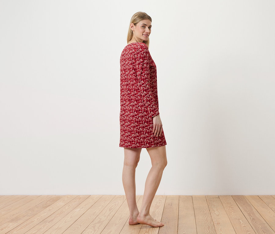 Frau steht seitlich und trägt ein rotes Kleid mit Muster.