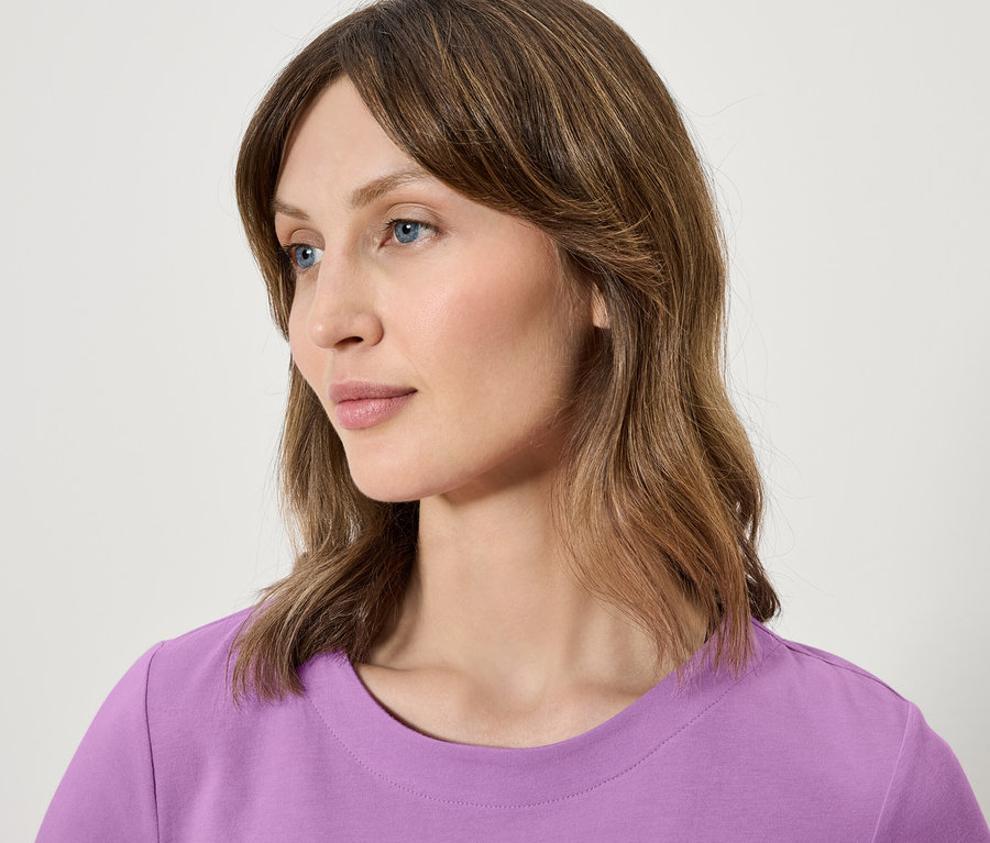 Detailporträt einer Frau mit braunen Haaren und blauen Augen, die ein lila T-Shirt trägt.