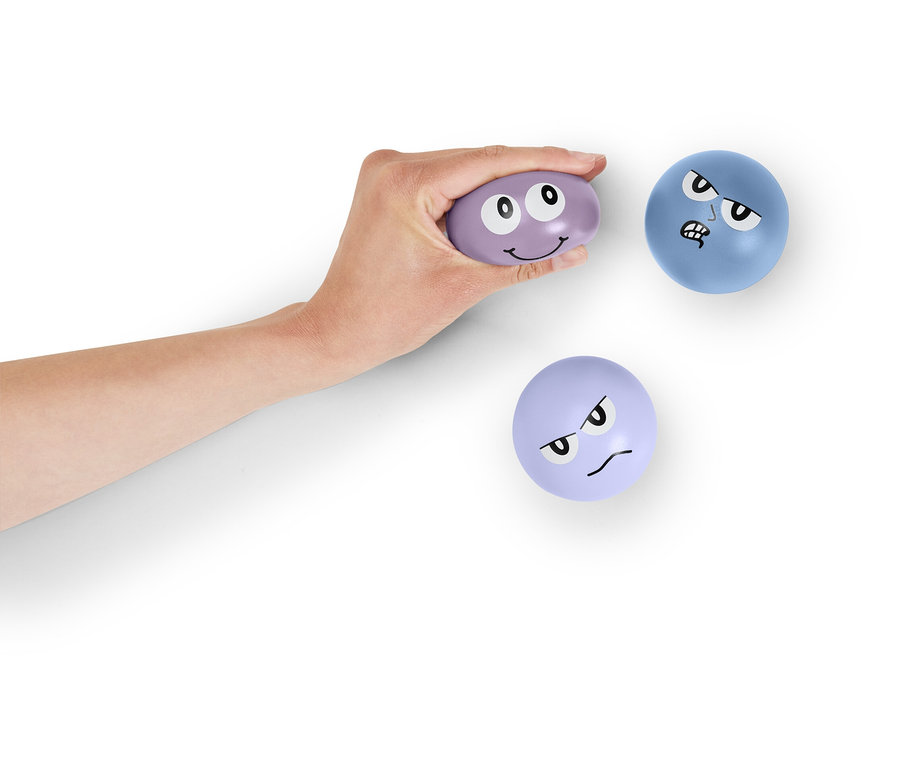 Eine Hand hält einen lila Ball mit Gesicht. Zwei weitere Bälle mit Gesicht liegen auf weißem Hintergrund.
