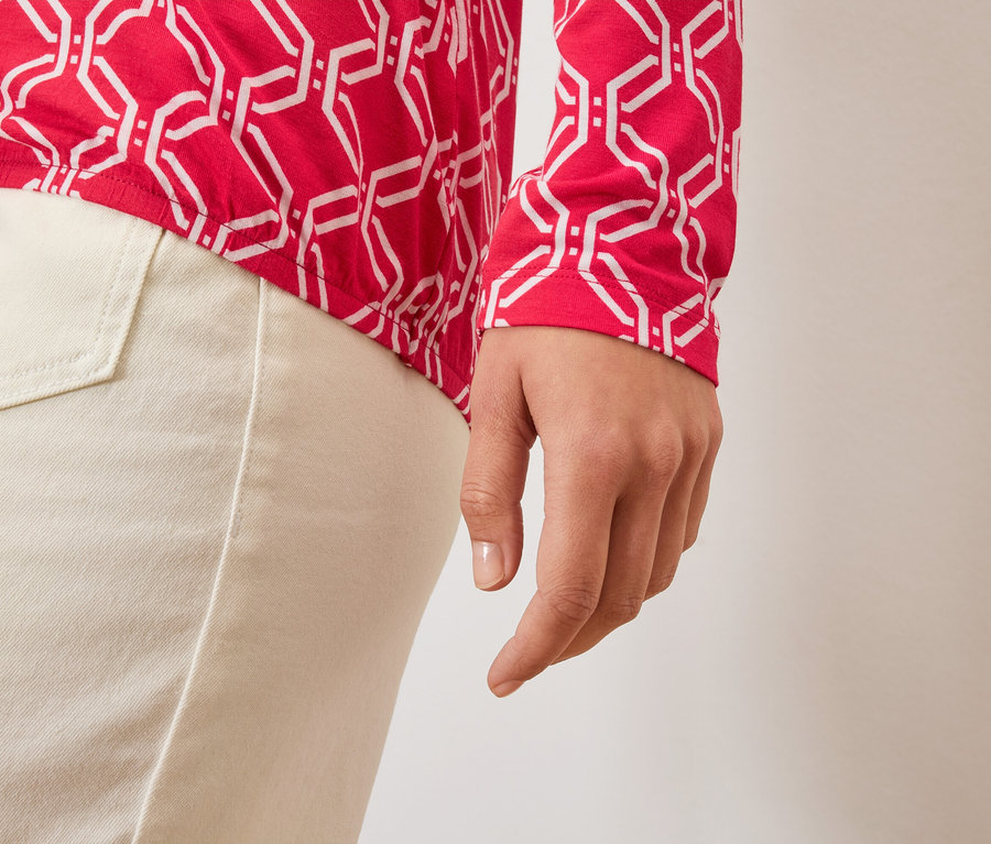 Detailaufnahme einer Damenhand, eines rot-weißen Oberteils und einer hellen Hose.