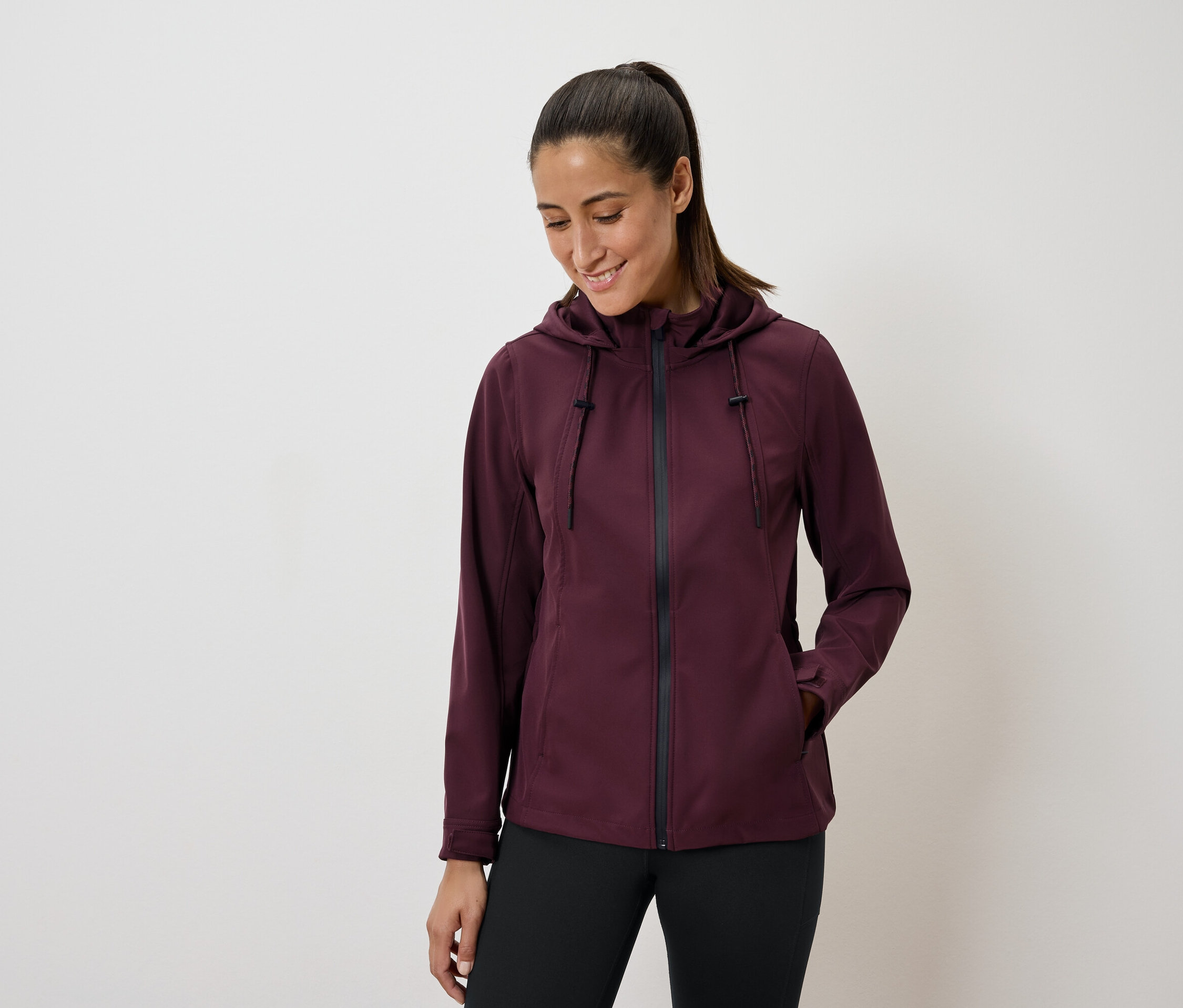 Frau trägt eine burgunderfarbene Kapuzenjacke und schwarze Leggings.