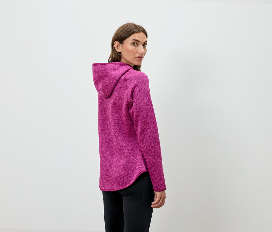 Frau blickt über die Schulter und trägt einen pinkfarbenen Kapuzenpullover und eine schwarze Hose.