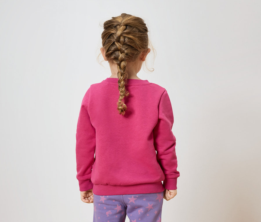 Mädchen mit Zopf steht mit dem Rücken zur Kamera, trägt ein pinkes Sweatshirt und lila Hosen mit Sternen.