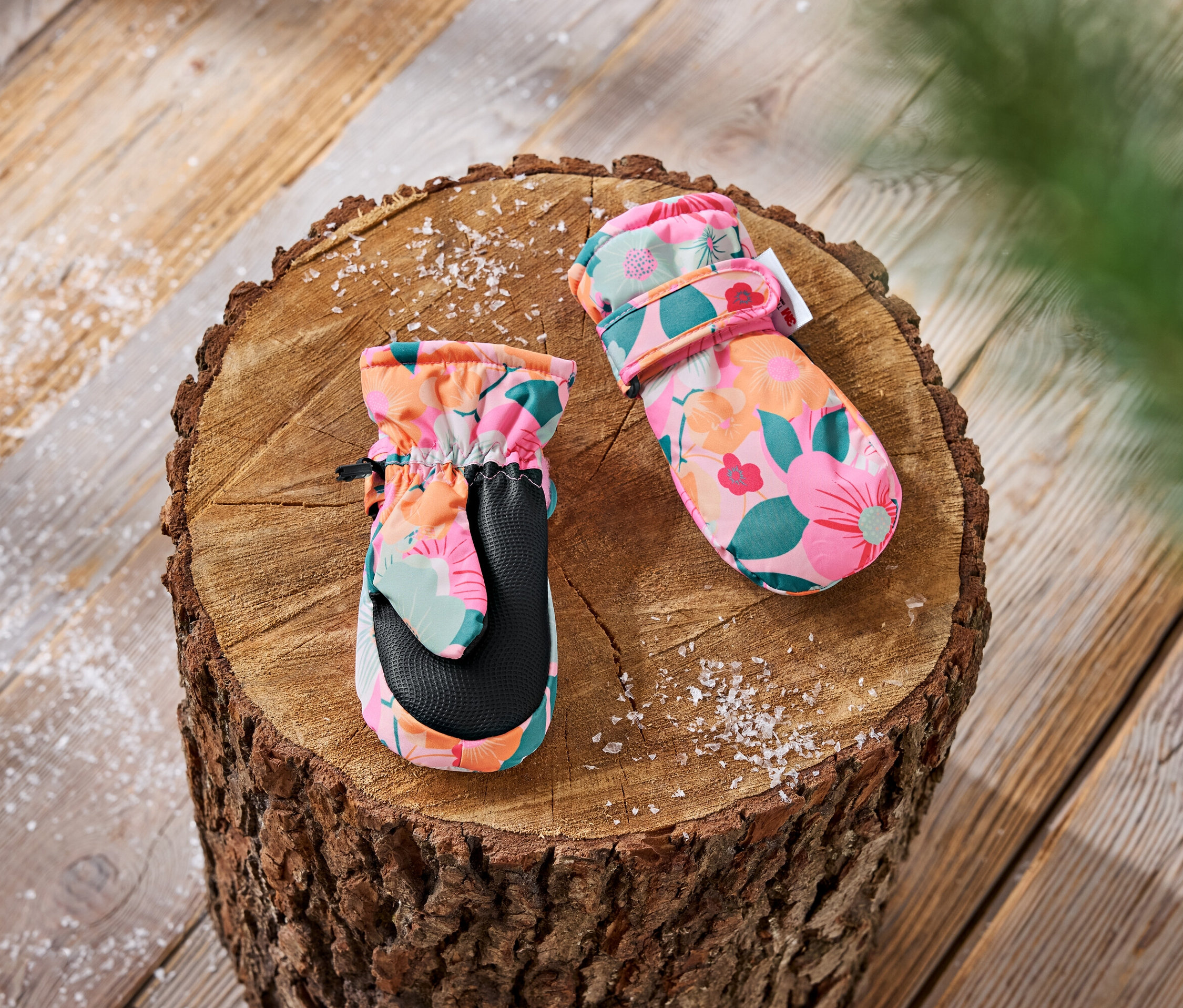 Kinderfäustlinge mit Blumenmuster liegen auf einem Holzscheit.