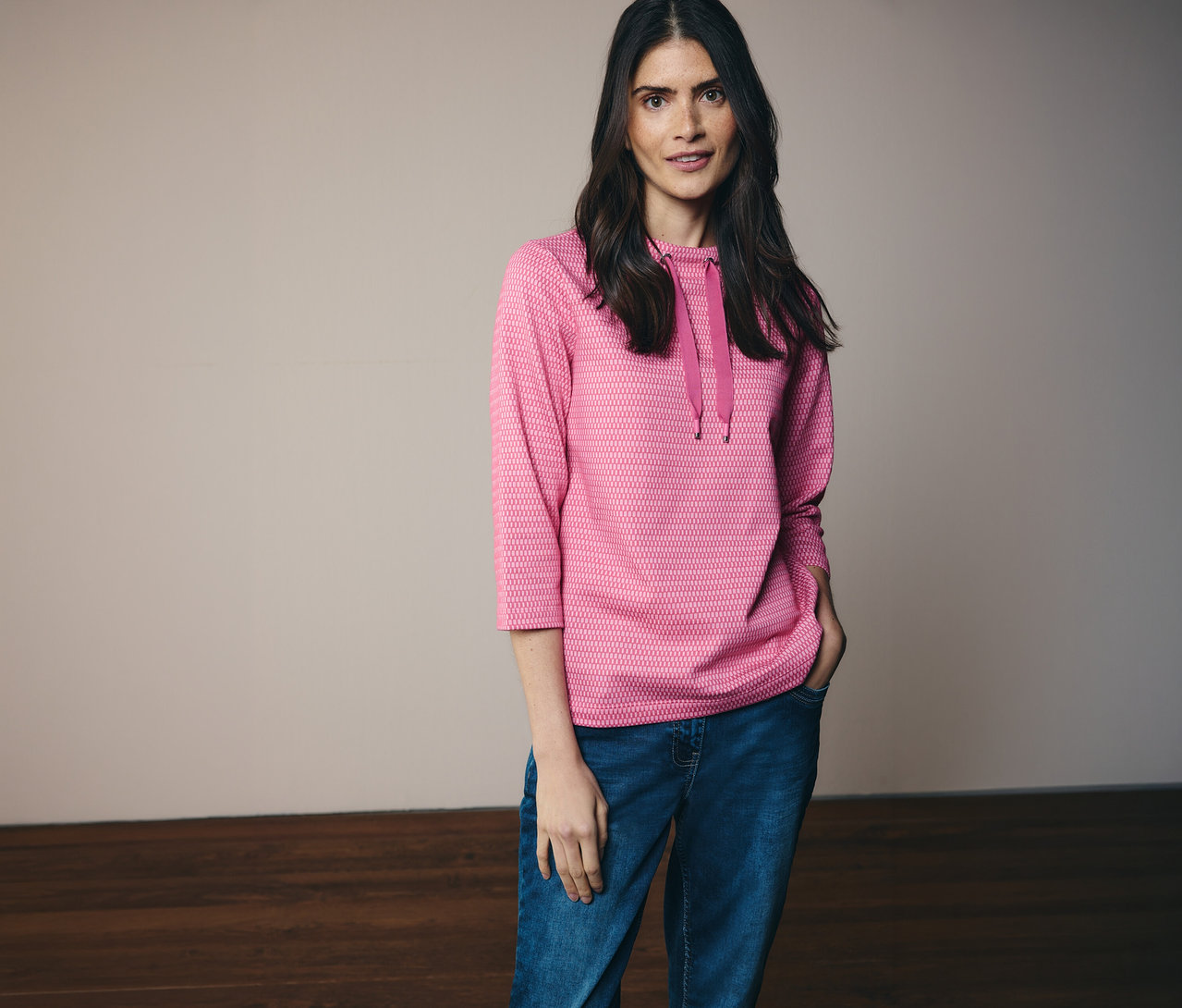 Frau mit Jeans und pinkem CECIL Sweatshirt mit Kapuze und 3/4 Ärmeln, eine Hand in der Hosentasche.