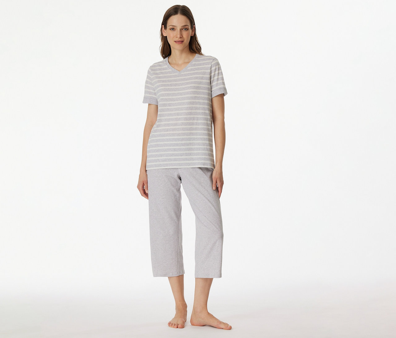 Frau trägt SCHIESSER 3/4-Pyjama mit grau-weiß gestreiftem T-Shirt und grauer 3/4-Hose vor weißem Hintergrund.