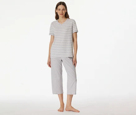 Frau trägt SCHIESSER 3/4-Pyjama mit grau-weiß gestreiftem T-Shirt und grauer 3/4-Hose vor weißem Hintergrund.