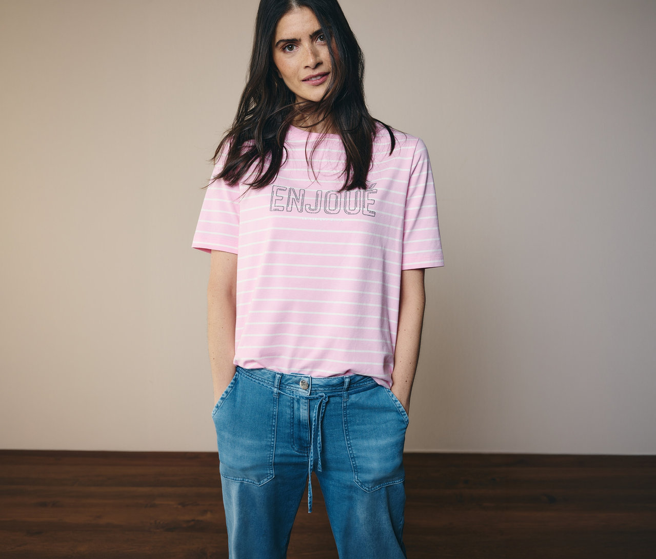 Frau mit Jeans und einem rosa-weiß gestreiften CECIL Shirt mit dem Wort ENJOUE.