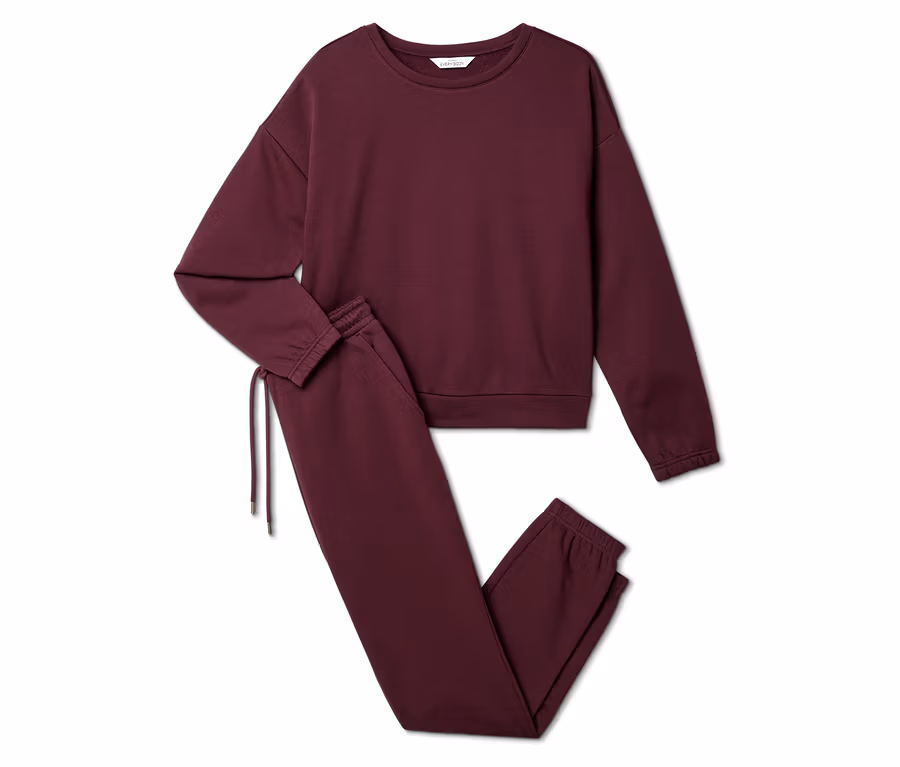 Burgunderfarbenes Set aus Sweatshirt und Jogginghose liegt auf weißem Grund.