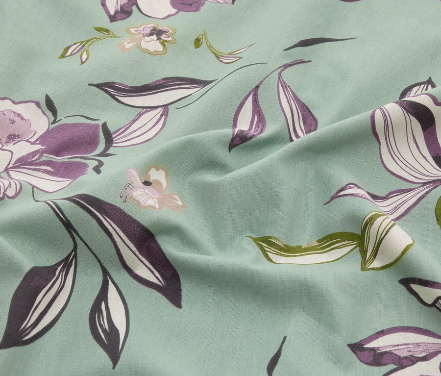 Nahaufnahme eines mintfarbenen Stoffes mit Blumenmuster in Lila-, Weiß- und Grüntönen.