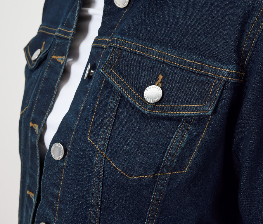 Nahaufnahme einer blauen Jeansjacke mit silbernen Knöpfen und einer Brusttasche.