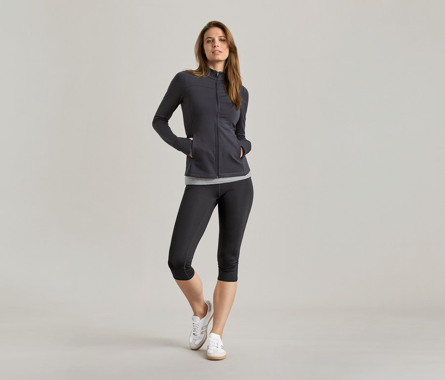 Frau in Sportbekleidung mit 2 schwarzen/grauen Tops unter einer Jacke.